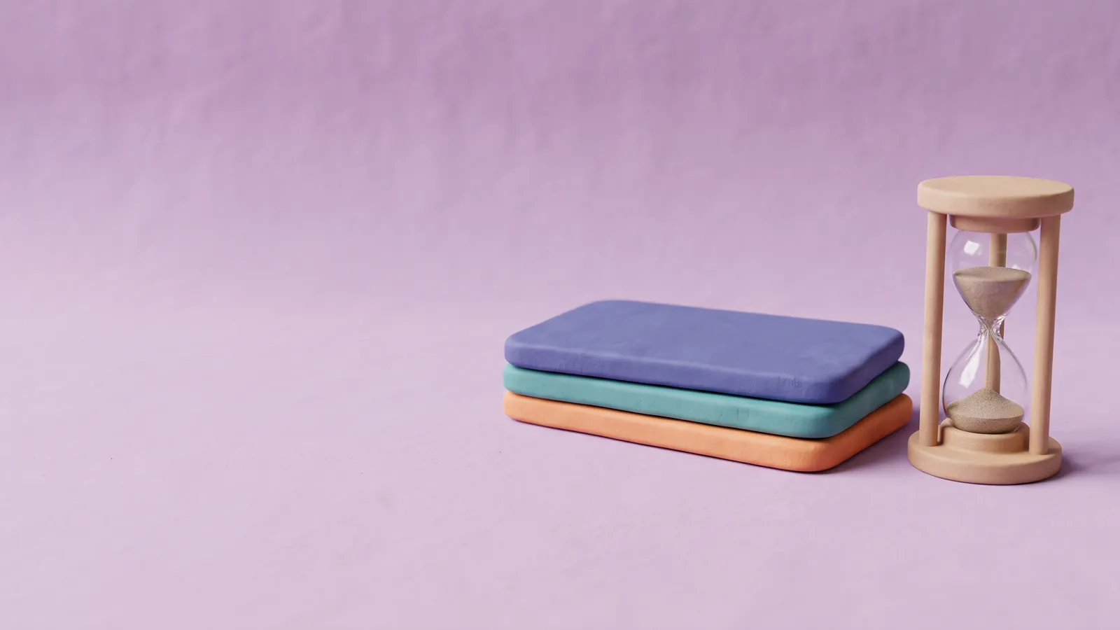 Drei flache Karten aus mattem Ton in Indigo, Türkis und Orange, daneben eine Sanduhr aus Holz